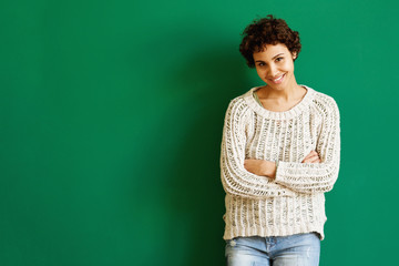 smiling african american woman standing against green wall with arms crossed