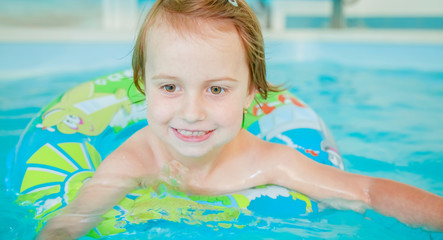 Funny portrait of happy cute little child girl playing with colorful ring in swimming pool.
