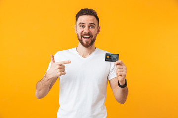 Happy young handsome man posing isolated over yellow wall background holding credit card.