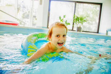 Funny portrait of pretty little child girl with colorful ring in swimming pool.