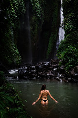 Fototapeta premium Back view of beautiful woman bathing and relaxing in natural swimming pool before waterfall in natural park on tropical island. beautiful waterfall in the Bali, Indinesia