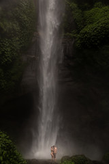 Young couple enjoying the freshness of nature under a waterfall in the tropics. The young pair hugging and kissing under waterfall.