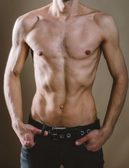 Naked torso of a young, slim, pumped-up man on a beige background. Tight naked attractive man in black jeans.