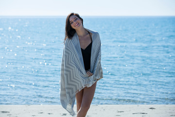 Pretty young girl wrapped in beach towel poses to camera. Full length photo shoot and wonderful hair. Healthy, beauty and summer holiday concept.