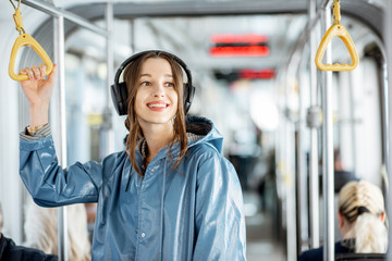 Young stylish woman enjoying trip in the public transport, standing with headphone while moving in...