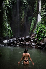 Back view of beautiful woman bathing and relaxing in natural swimming pool before waterfall in natural park on tropical island. beautiful waterfall in the Bali, Indinesia