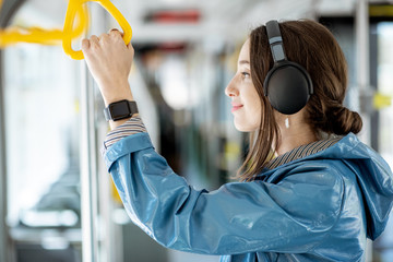 Young woman holding handle while moving in the modern tram. Happy passenger enjoying trip at the...