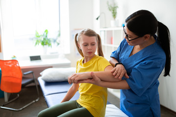 Caring long-haired nurse in blue uniform asking little girl about feelings