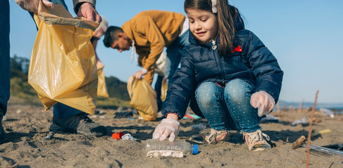 Little happy girl with volunteers picking up trash on the beach