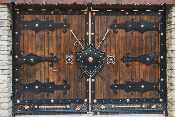 Wooden gates with forged hinges. A shield and a sword hang on the gate.