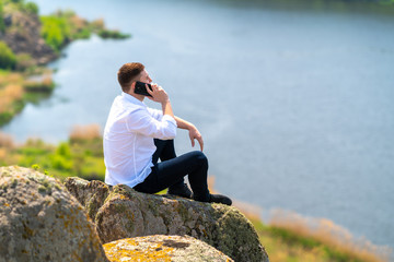 Young man sitting on a rock chatting on a mobile