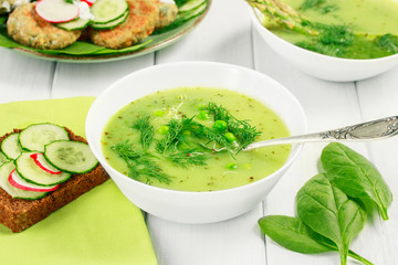 Healthy food vegetarian soup with asparagus and spinach, green peas and bread with vegetables on a white table.