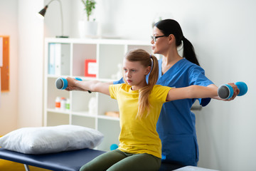 Diligent light-haired girl in yellow t-shirt repeating postures of active nurse