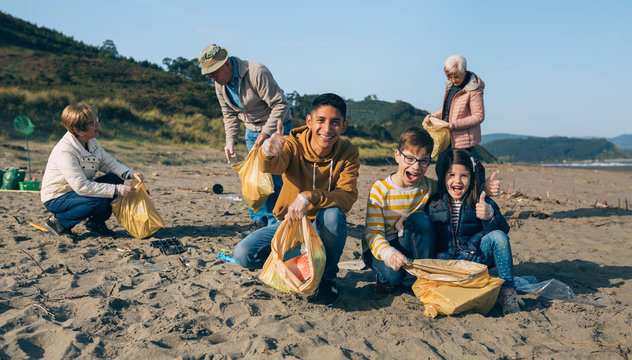 Young Man And Children Posing While Picking Up Trash With Group Of Volunteers On The Beach