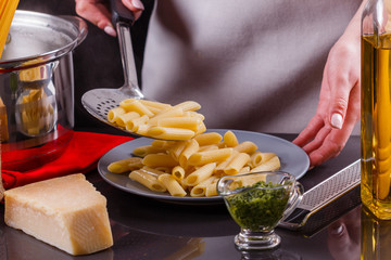 young woman in a gray apron is preparing pasta pesto