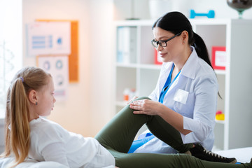 Careful pleasant long-haired doctor rubbing different parts of the leg