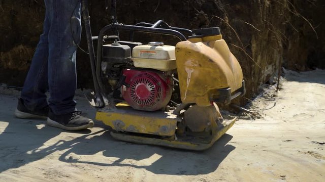 partial shot of man working with vibrating plate compactor on sand surface