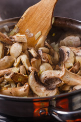 young woman in a gray apron roasts mushrooms in a frying pan