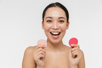 Pretty asian woman with healthy skin posing naked isolated over white wall background holding makeup sponge.