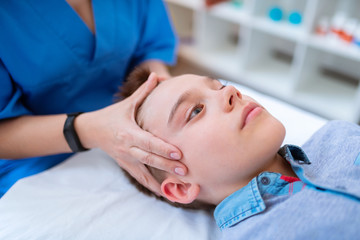 Obraz na płótnie Canvas Tranquil short-haired boy calmly lying during relaxing head massage