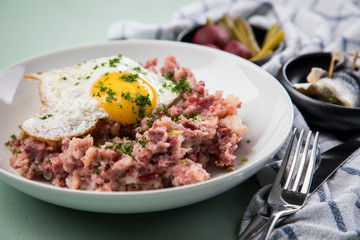 Norddeutscher Hamburger Labskaus mit Rindfleisch Corned Beef, Rote Beete, Kartoffeln, Saure Gurken, Spiegelei und Rollmops auf Teller