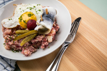 Norddeutscher Hamburger Labskaus mit Rindfleisch Corned Beef, Rote Beete, Kartoffeln, Saure Gurken, Spiegelei und Rollmops auf Teller