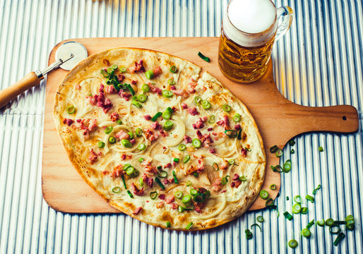 Tarte flambe or Flammkuchen with bacon and onions on wooden cutting board with a glass of beer