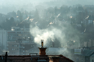 Chimney smokestack on oId appartment building roof top emitting white smoke fume clouds with urban...