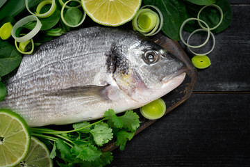 Fresh dorada fish with herbal, onion, parsley and lime on a cutting board on black background, top view and copy space