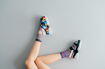 Beautiful female legs in mismatched trendy socks posing in two different fashionable high wedge leather sandals on gray background. Odd disargonized  young girl wearing high sole summer stylish shoes.