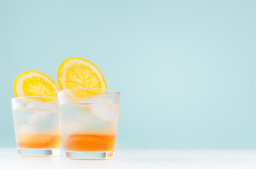 Fresh shot cocktails with oranges liquor, slice orange, ice cubes in misted shot glass on white wood table and blue color wall.