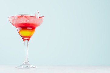 Exotic striped alcohol citrus red and yellow cocktail with ice cubes in rich wet wineglass on  pastel green background.