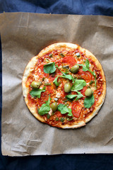 Homemade vegetarian pizza with tomato sauce, two types of cheese, tomatoes, peppers, arugula, olives and herbs. Top view.