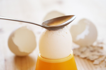 Breaking of a shell of the boiled chicken egg with a spoon at breakfast