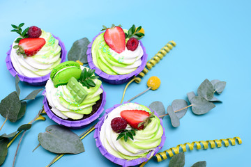 cupcakes with whipped cream decorated chocolate bar, strawberry ,macaroons on blue background. Picture for a menu or a confectionery catalog. with space for text. decorated with eucalyptus leaves.