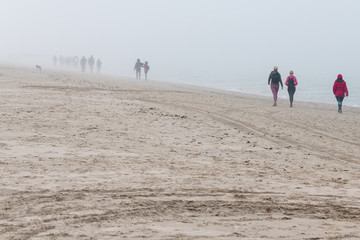 Fototapeta na wymiar Walkers at Baltic sea in foggy day.