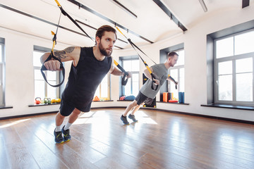 Fototapeta na wymiar Two fit strong athletic male friends are training together with trx in the gym. Concept of strength training and resistance exercises