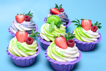 cupcakes with whipped cream decorated chocolate bar, strawberry ,macaroons on blue background. Picture for a menu or a confectionery catalog. with space for text.