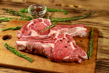 Raw fresh beef rib eye steaks on bone with spices and rosemary on wooden table