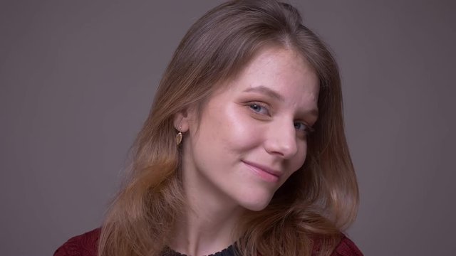 Portrait of young female student ogling and flirting with camera playfully on gray background.