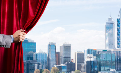 Modern business cityscape behind curtain opened by businessman hand