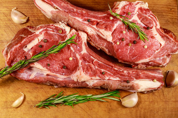 Raw fresh beef rib eye steak on bone with spices, garlic and rosemary on wooden table. Top view