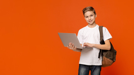 Teenage boy with backpack using laptop, orange background