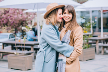 Best girlfriends hug kiss and love.. Adult emotional women sisters dressed in stylish beige and blie coat, brown hat. Hipster. Warm toning. The concept of true friendship.