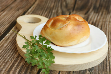 Tradisional russian Pie with onion and egg on a white plate on a round cutting board laying on a wooden table, side view, horizontal