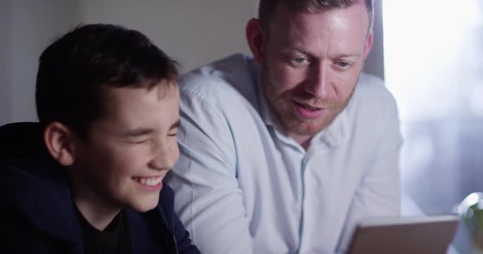 4K Happy father & son spending time together at home, internet browsing on digital tablet. Slow motion.