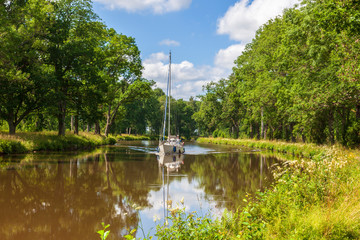 Sailboat on a beautiful canal lined with lush trees
