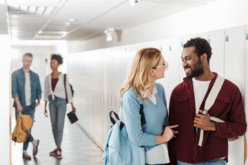 smiling multiethnic students looking at each other in corridor in college