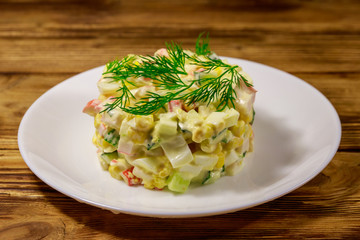 Salad with crab sticks, sweet corn, cucumber, eggs and mayonnaise on wooden table