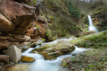 Colorful amphitheater of a mountain creek and a waterfall, during spring in a forest, photographed from a low angle perspective with blur motion water
